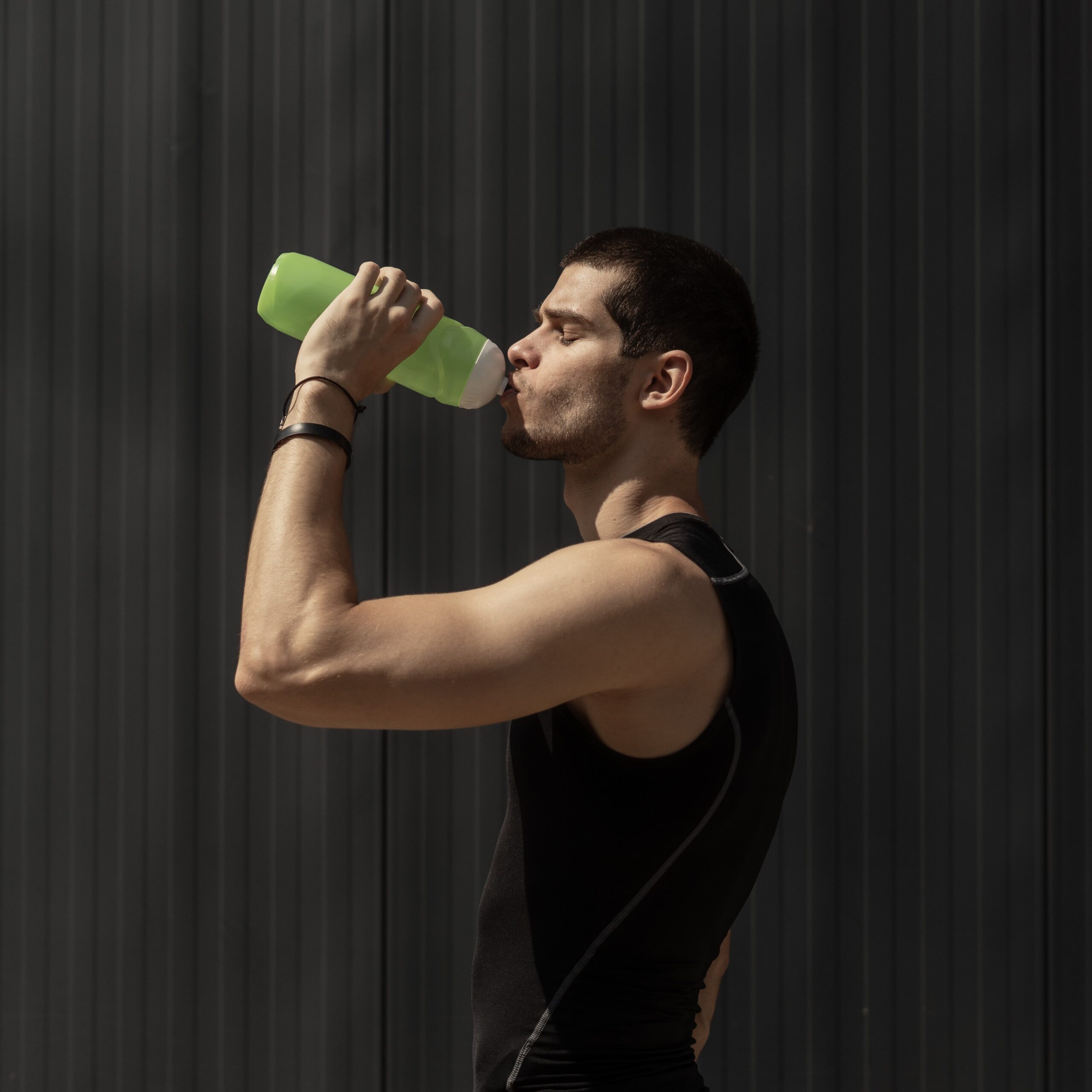 Sport model man drinking water from a plastic bottle on gray background with copy space. Portrait muscular man taking a break to hydrate his body after training.